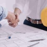This is an image symbolizing the trust that is earned when a business owner gets a surety bond. It shows two men shaking hands over a project blueprint.